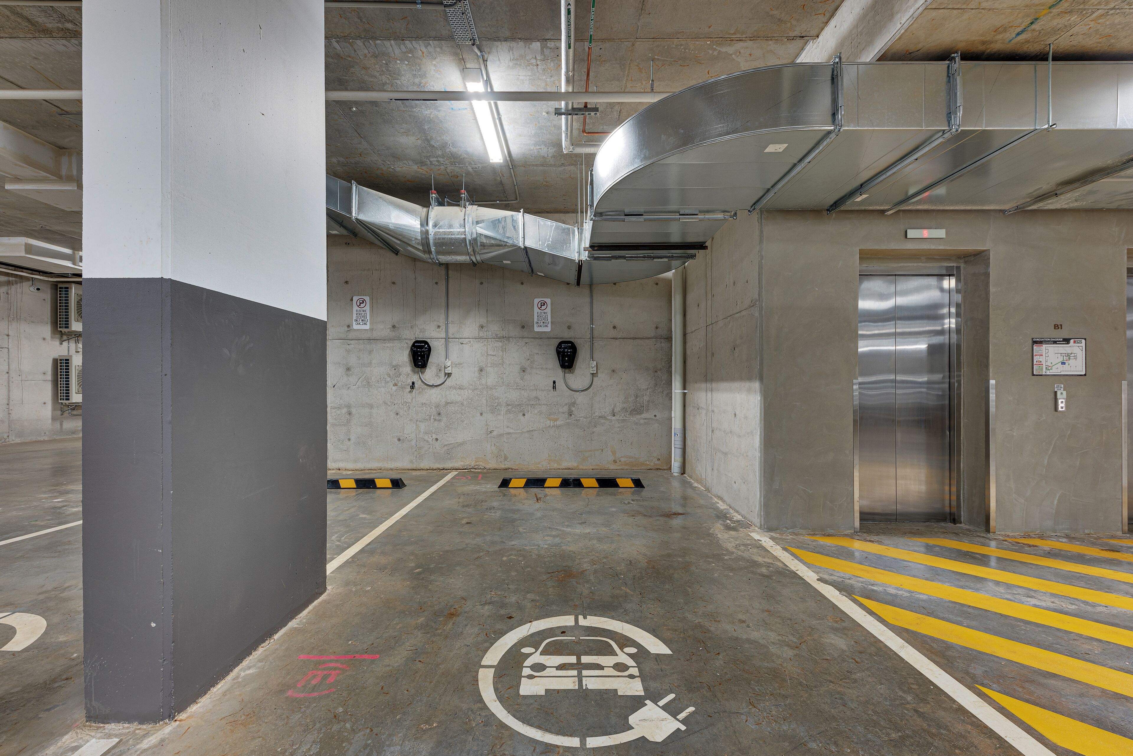 A parking garage with concrete pillars, a car charging station, and an elevator.