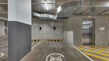 A parking garage with concrete pillars, a car charging station, and an elevator.
