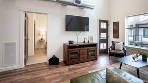 Ein modernes Wohnzimmer mit Holzdielenboden, einem an der Wand befestigten Flachbildfernseher, einer dunklen Holzunterhaltungseinheit, einem Ledersofa und einem Fenster mit natürlichem Licht.