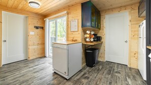 Cocina compacta con paredes de madera, lavavajillas, cafetera y cubo de basura.