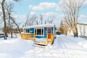 A small, single-story cabin with a blue exterior and a red door, surrounded by snow-covered ground and leafless trees. - 🏝 Sandy Hooked  2Bed1Bath Remodelled Pine Cottage (Sandy Hook)