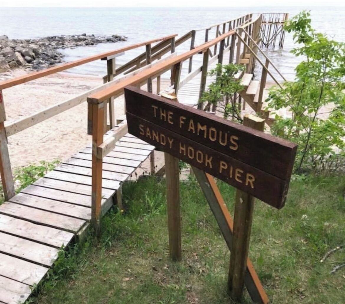A wooden sign with the text "The Famous Sandy Hook Pier" at a beachside location.