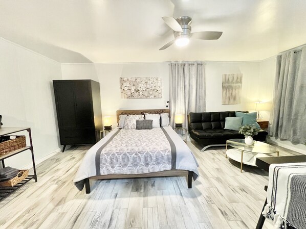 A modern bedroom with a large bed, a sofa, a desk, and a wardrobe.