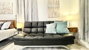 Una sala de estar moderna con un sofá de cuero negro, una mesa de centro de vidrio y piso de madera.