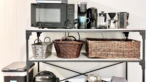 Una cocina con microondas, tostadora, cafetera y diversos utensilios de cocina en estantes.