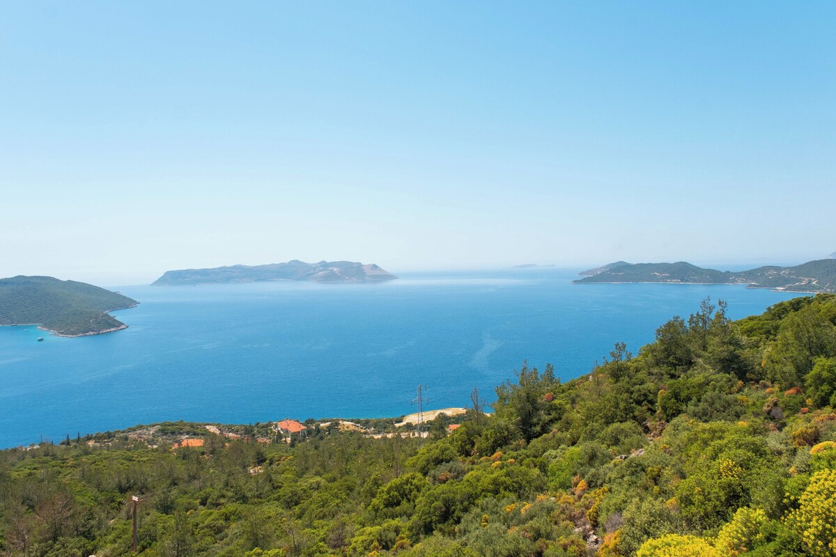 A coastal landscape with a clear view of the sea, hills, and a small settlement with buildings.