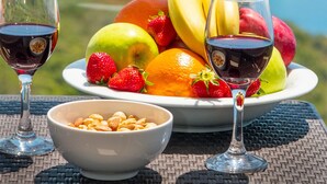 A table with a fruit bowl, a bowl of nuts, and two wine glasses, set against a scenic coastal backdrop. - Golden Rose Suit Pension (Kas)