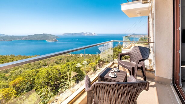 A balcony with wicker furniture, a table with cups, and a scenic view of the sea and hills. - Golden Rose Suit Pension (Kas)