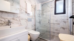 A modern bathroom with a marble backsplash, a glass shower enclosure, and a white sink. - Golden Rose Suit Pension (Kas)