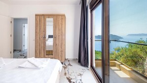 A bedroom with a large bed, a wooden wardrobe, and a balcony with a view of the sea. - Golden Rose Suit Pension (Kas)
