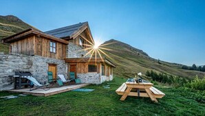 Ein rustikales Berggemütliches Ferienhaus mit Natursteinfundament, Holzfassade und einer Terrasse mit Liegestühlen.