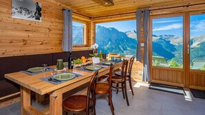 Ein Essbereich mit Holzboden, ein Tisch für vier Personen, große Fenster mit Blick auf die Berge und ein gerahmtes Bild an der Wand.