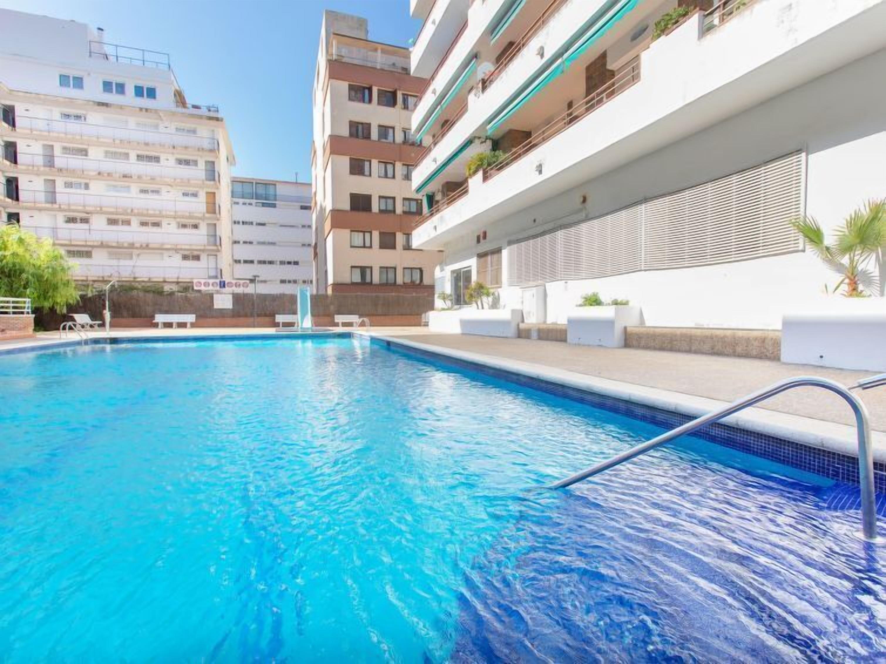 A swimming pool with a clear blue water, surrounded by a white building with balconies and a modern design.