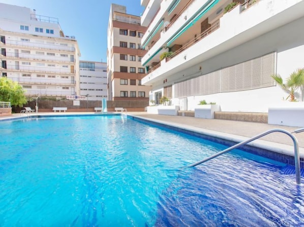 A swimming pool with a clear blue water, surrounded by a white building with balconies and a modern design.