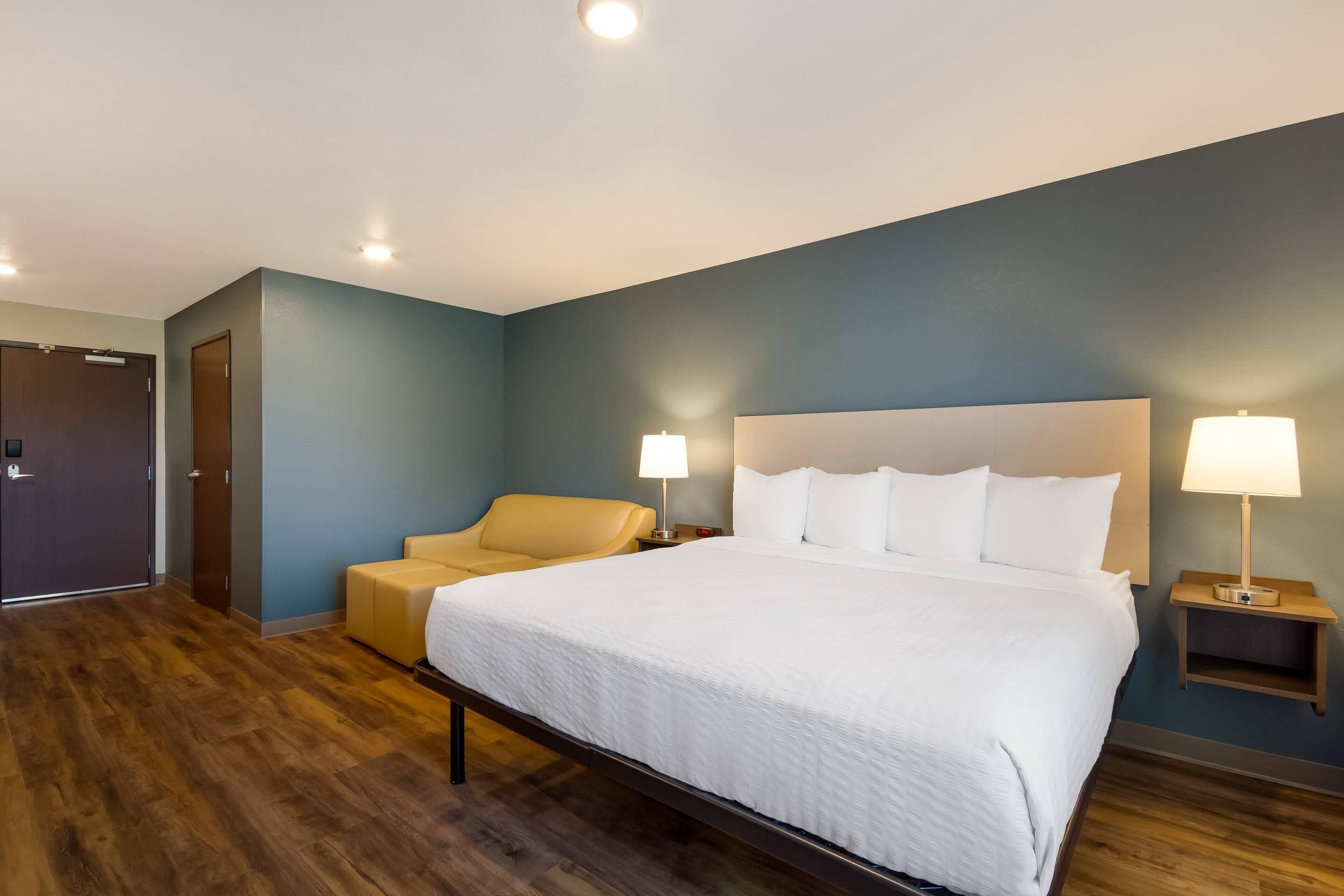 A hotel room with a large bed, two bedside lamps, a sofa, and a wooden floor.