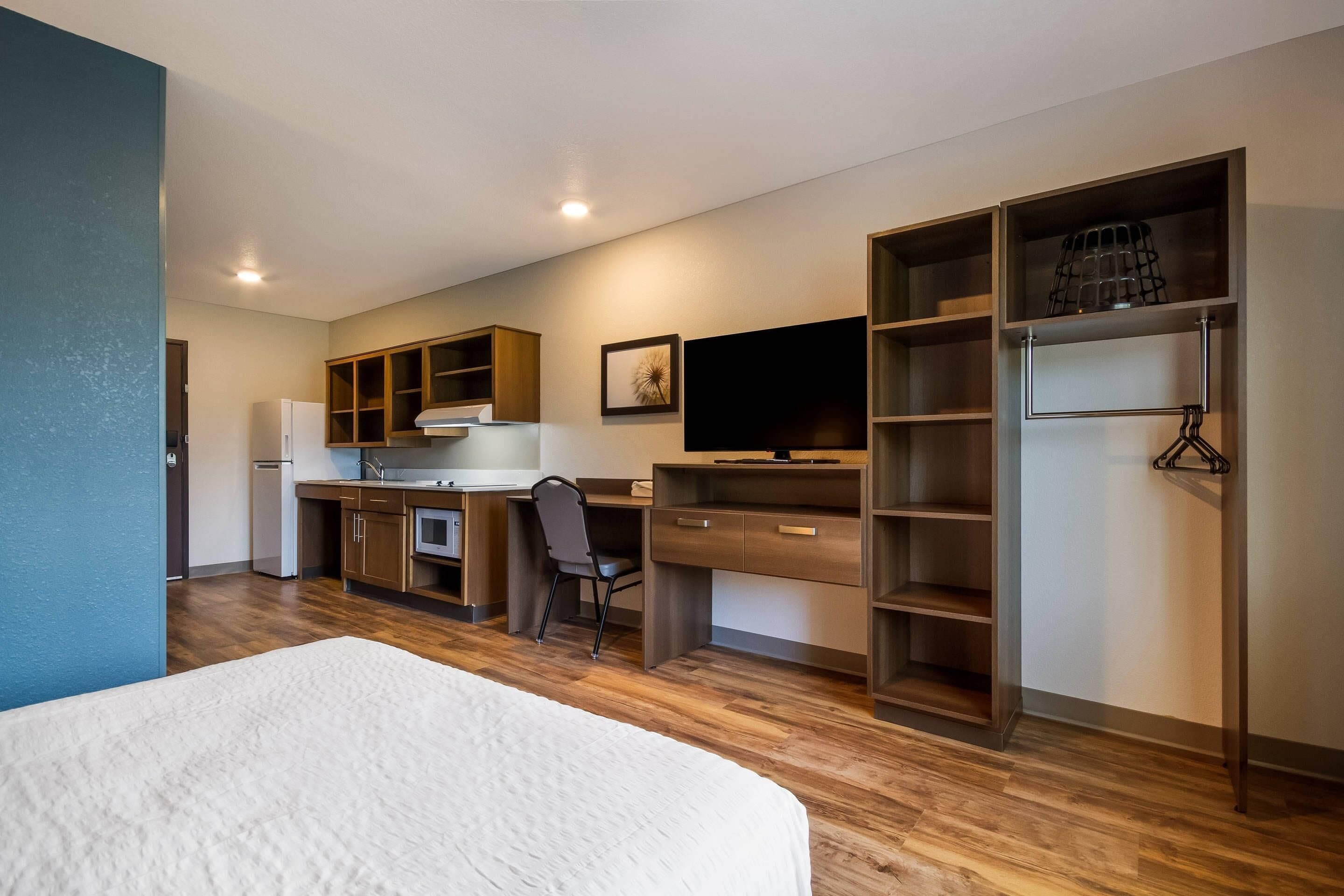 A modern hotel room with a bed, a desk, a chair, a television, and built-in shelving.