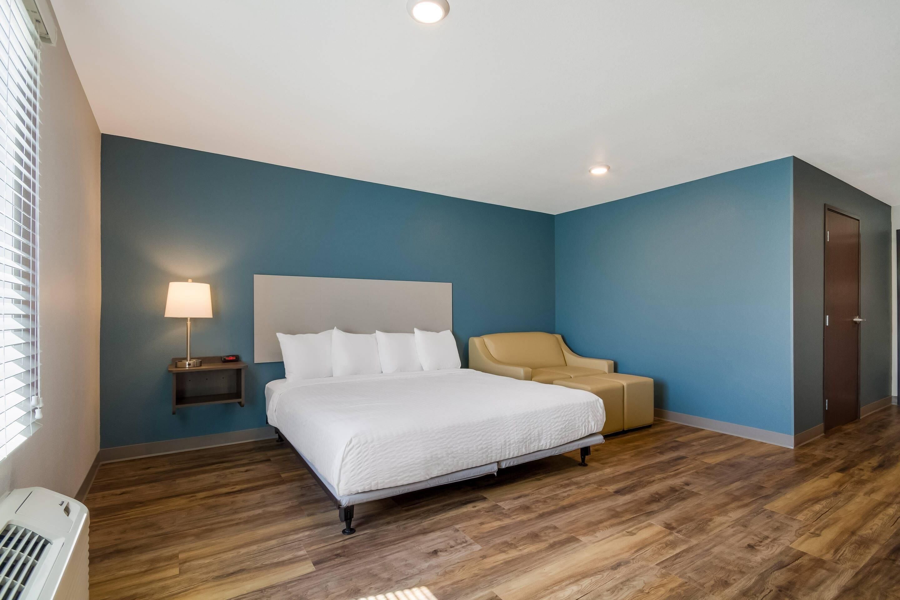 A hotel room with a large bed, a bedside table with a lamp, a chair, and a wardrobe.