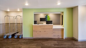A reception area with a wooden counter, a green accent wall, and a modern design. - Woodspring Suites Panama City Beach (Panama City Beach)
