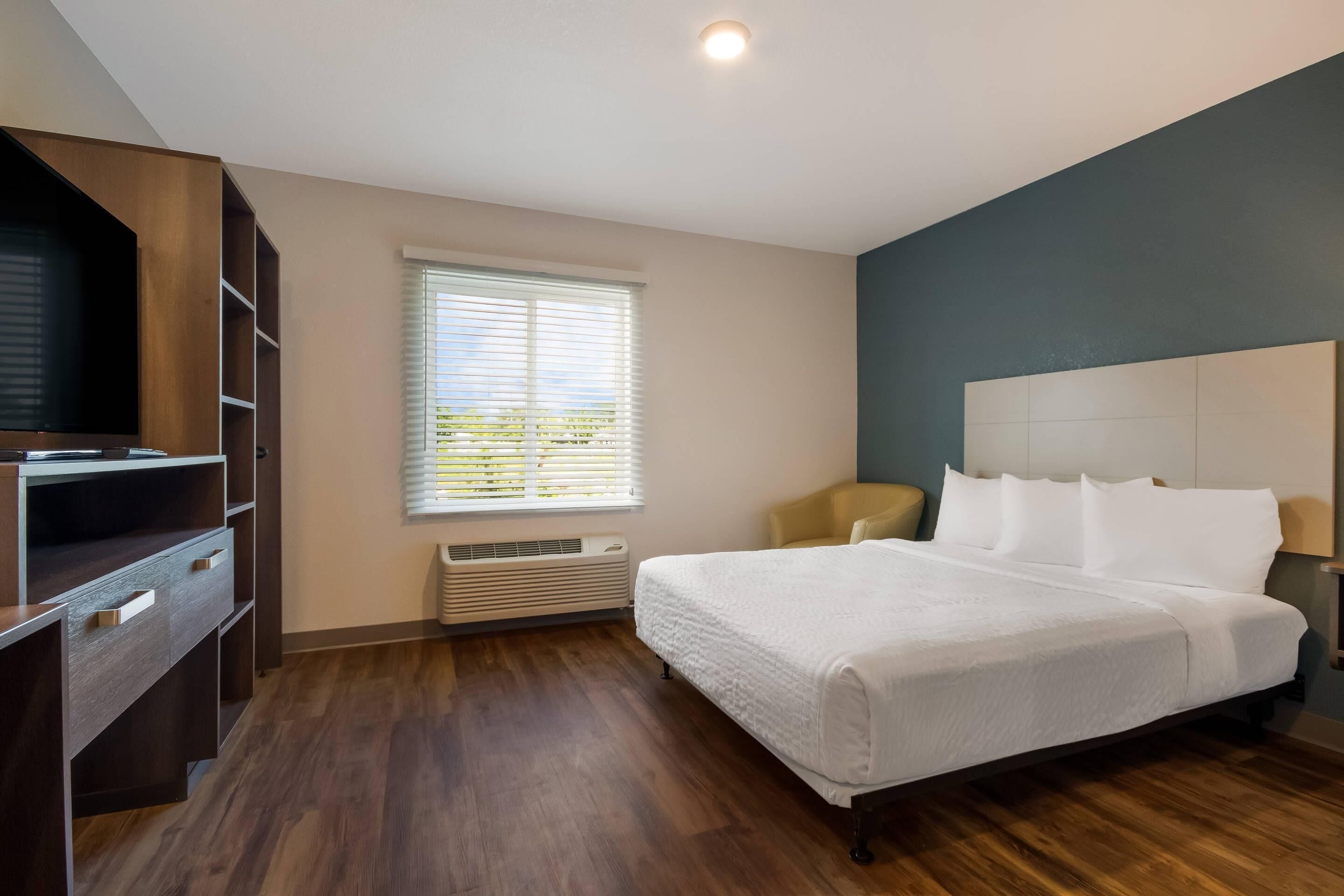 A hotel room with a large bed, built-in wardrobe, and a window with blinds.