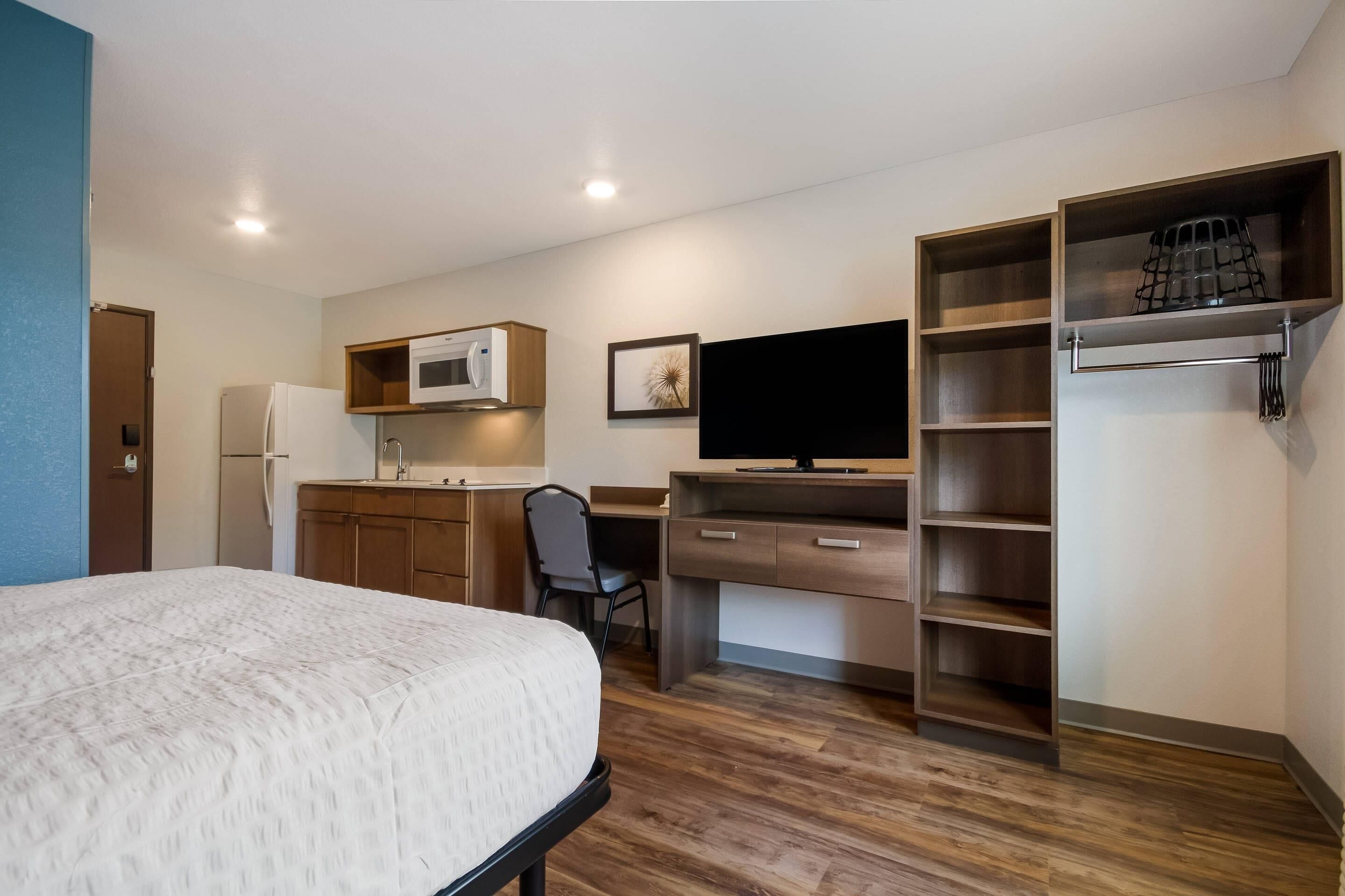 Una habitación de hotel compacta con cama, kitchenette, escritorio y armario empotrado.