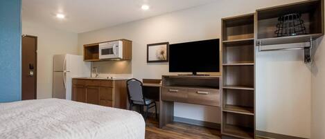 Una habitación de hotel compacta con cama, kitchenette, escritorio y armario empotrado.