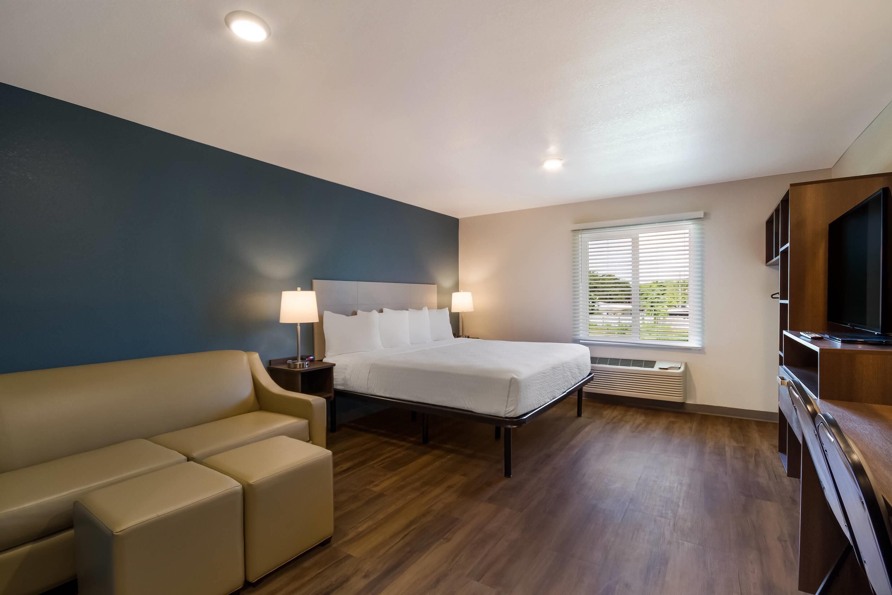 A hotel room with a bed, a sofa, a TV, and a window with blinds.