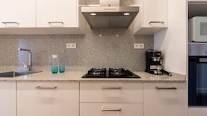 A modern kitchen with white cabinets, a granite countertop, a gas stove, a coffee maker, and a stainless steel range hood. - Atlantis by Interhome (Segur de Calafell)