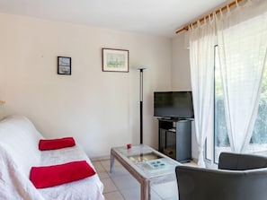 Moderni olohuone, jossa on sohva, sohvapöytä, televisio ja ikkuna, jossa on verhot.