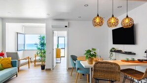 A modern living room with a dining area, large windows, and a flat-screen TV.