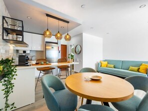 A modern kitchen with a dining area, featuring a round wooden table with four chairs, a coffee machine, and hanging pendant lights. - Sweet Ocean by Interhome (Armação de Pêra)