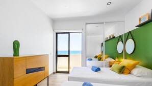 A modern hotel room with a large sliding door to the balcony, a wooden dresser, two beds with white linens, and green walls with circular mirrors.