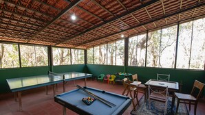 A pool table with billiard balls and cues, a ping pong table, and a dining area with chairs and a table. - Bamboo banks (Ootacamund)