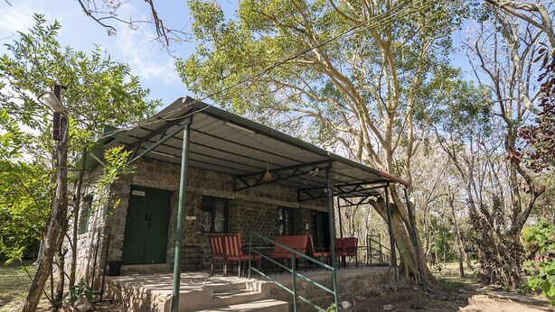 A stone building with a covered porch, outdoor seating, and a staircase leading to the entrance. - Bamboo banks (Ootacamund)