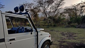 A white off-road vehicle parked in a grassy area with trees and hills in the background. - Bamboo banks (Ootacamund)