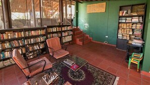 A cozy reading room with a sofa, armchairs, and a coffee table, surrounded by bookshelves filled with books. - Bamboo banks (Ootacamund)