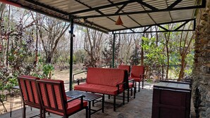 A covered outdoor seating area with red cushioned chairs and a table, surrounded by stone walls and trees. - Bamboo banks (Ootacamund)