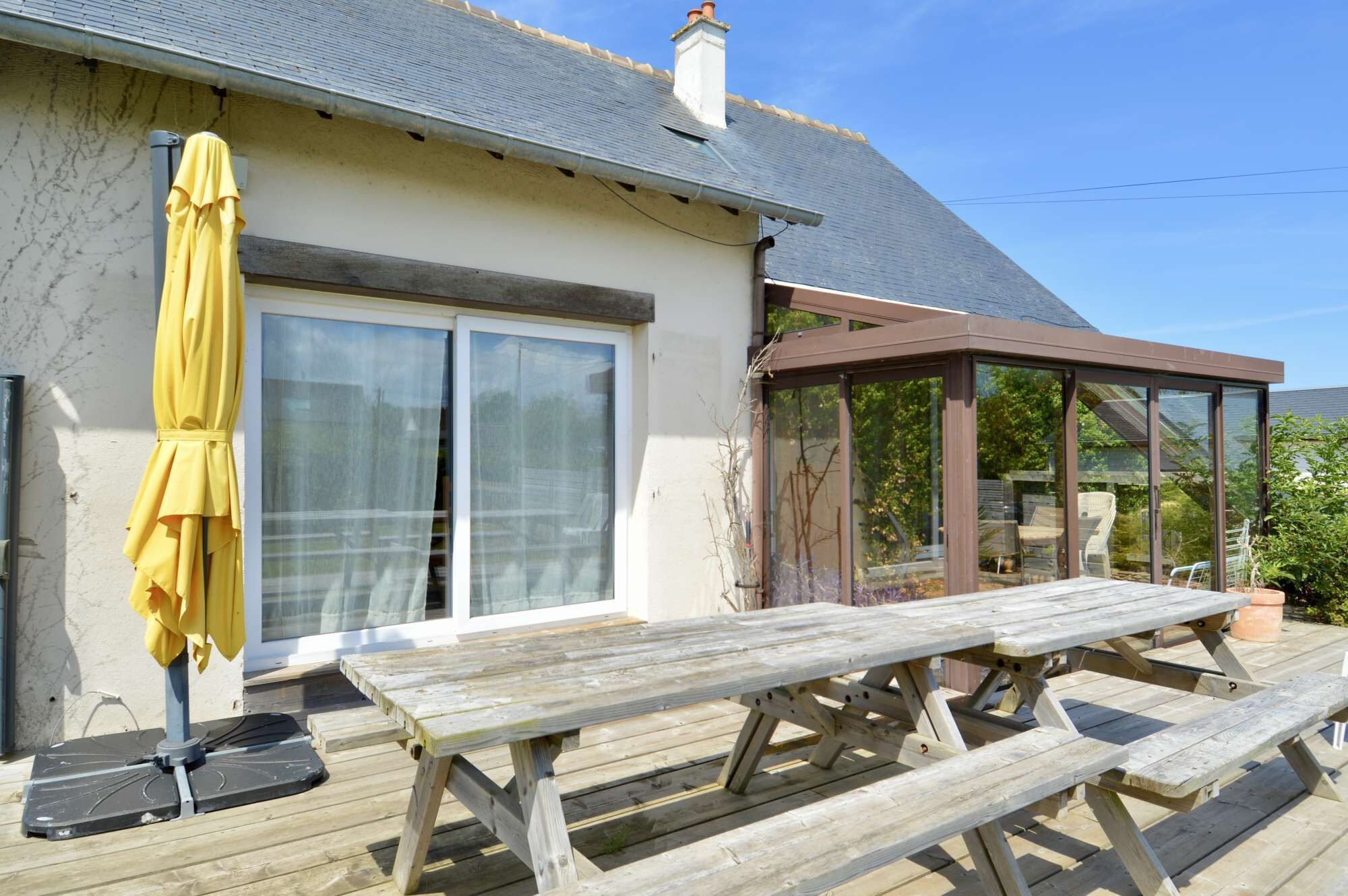 Een houten terras met picknicktafels, een gele parasol en een glazen patio.