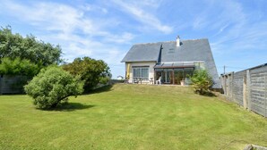 A house with a sloped roof, a patio with outdoor furniture, and a well-maintained lawn. - House (Asnelles)