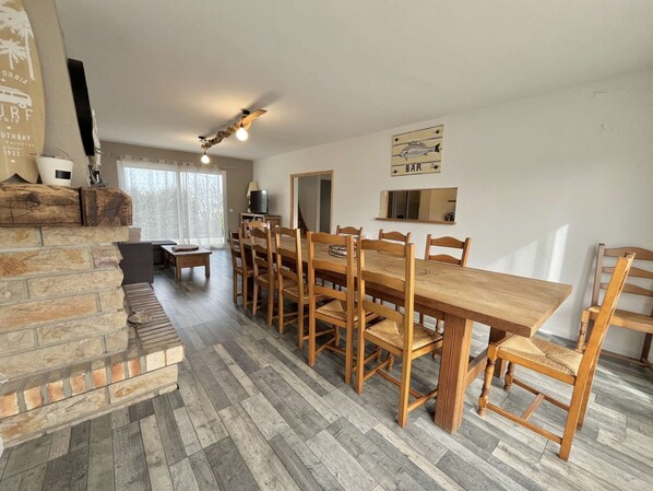 Un comedor con una mesa de madera larga y sillas, una chimenea de piedra y un ventilador de techo.