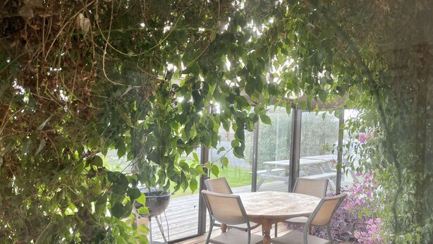 An outdoor patio with a table and chairs, surrounded by greenery and a view of the outdoors. - House (Asnelles)