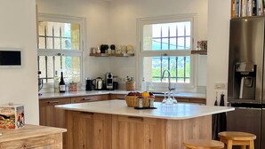 Una cocina con armarios de madera, una isla central, taburetes de bar, un refrigerador y una ventana con vistas a la vegetación.