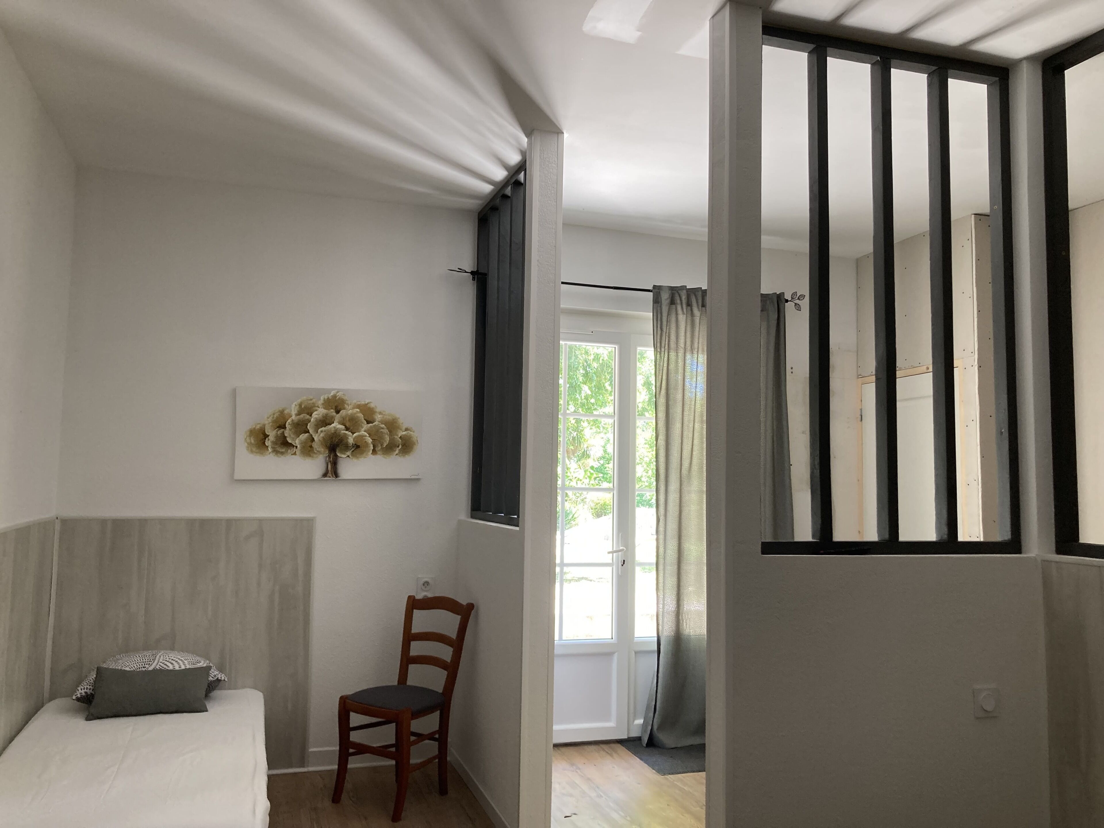 A bedroom with a bed, a chair, a wall-mounted artwork, and a window with curtains.