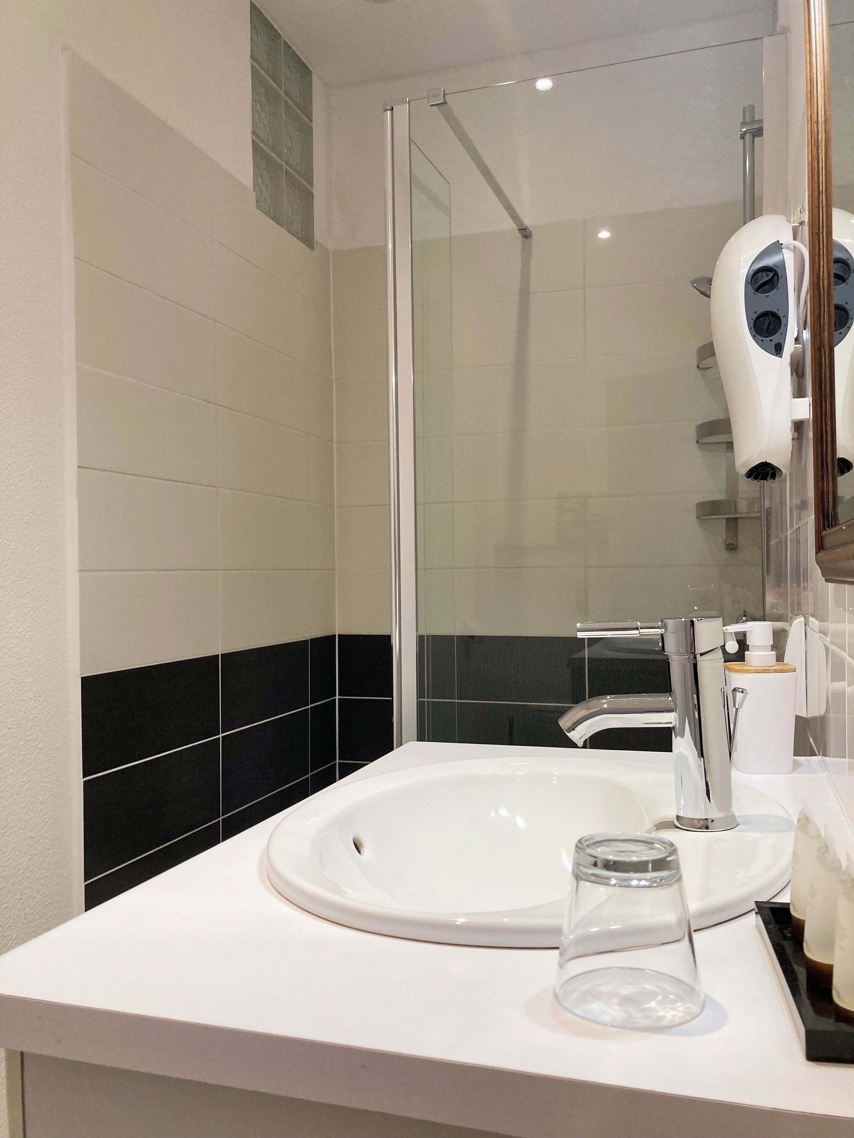 Un bagno moderno con un lavandino bianco, una cabina doccia in vetro e un asciugacapelli fissato alla parete.