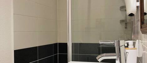 Un bagno moderno con un lavandino bianco, una cabina doccia in vetro e un asciugacapelli fissato alla parete.