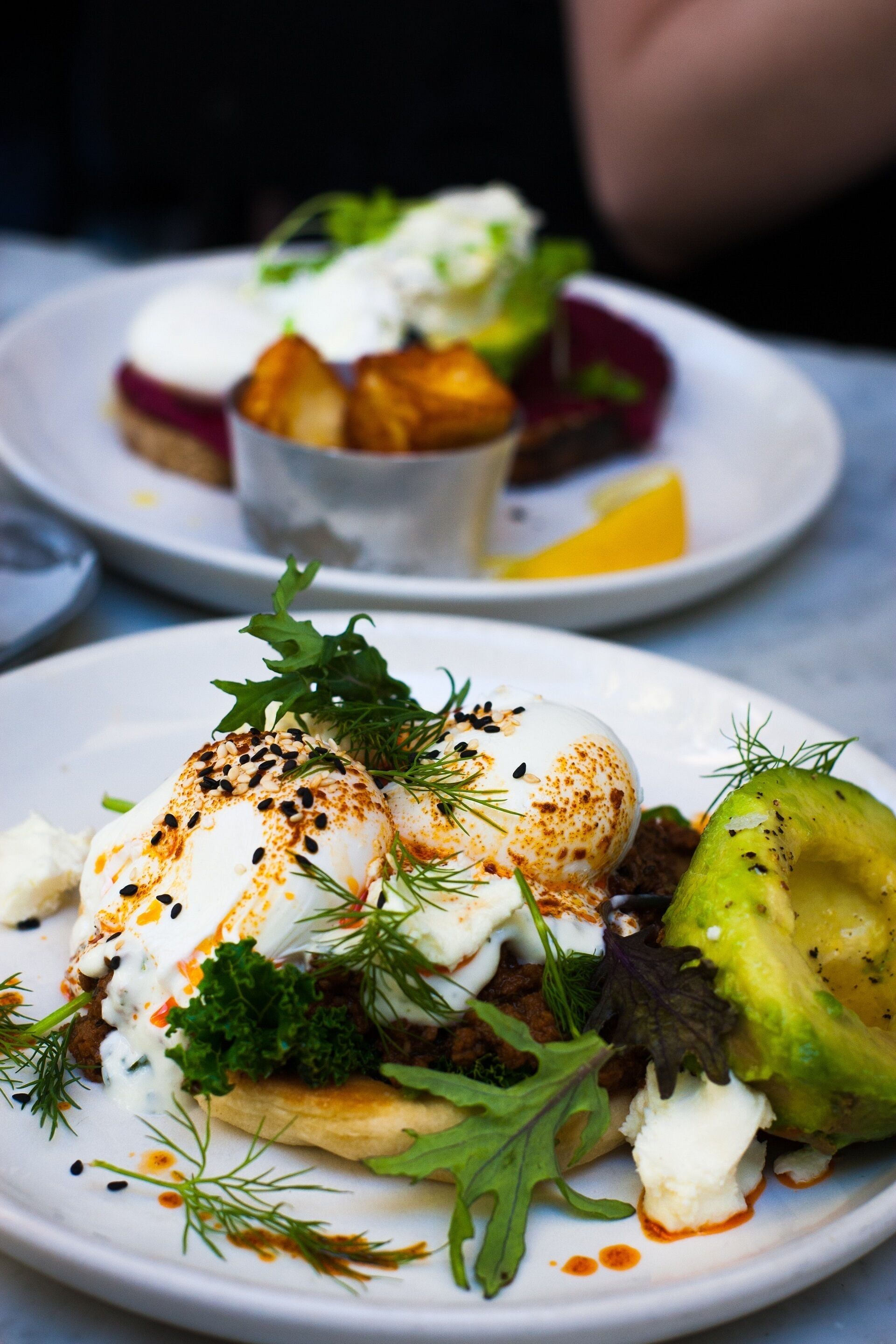 En tallrik med ett pocherat ägg, avokado, grönsaker och ett till pocherat ägg ovanpå en bädd av grönsaker.