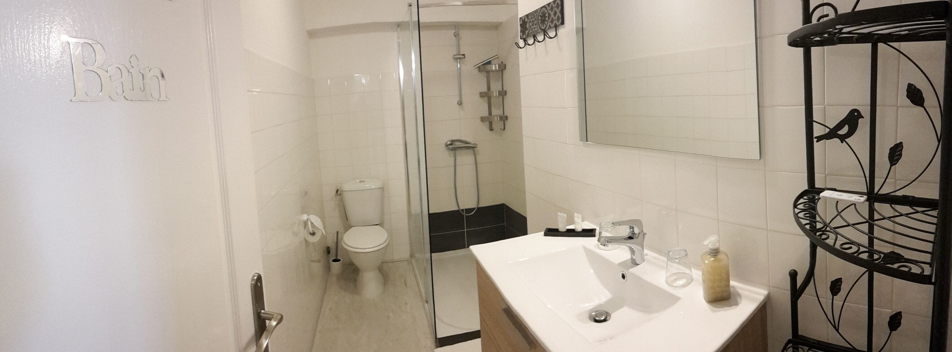A bathroom with a glass-enclosed shower, a toilet, a sink with a mirror, and a soap dispenser.