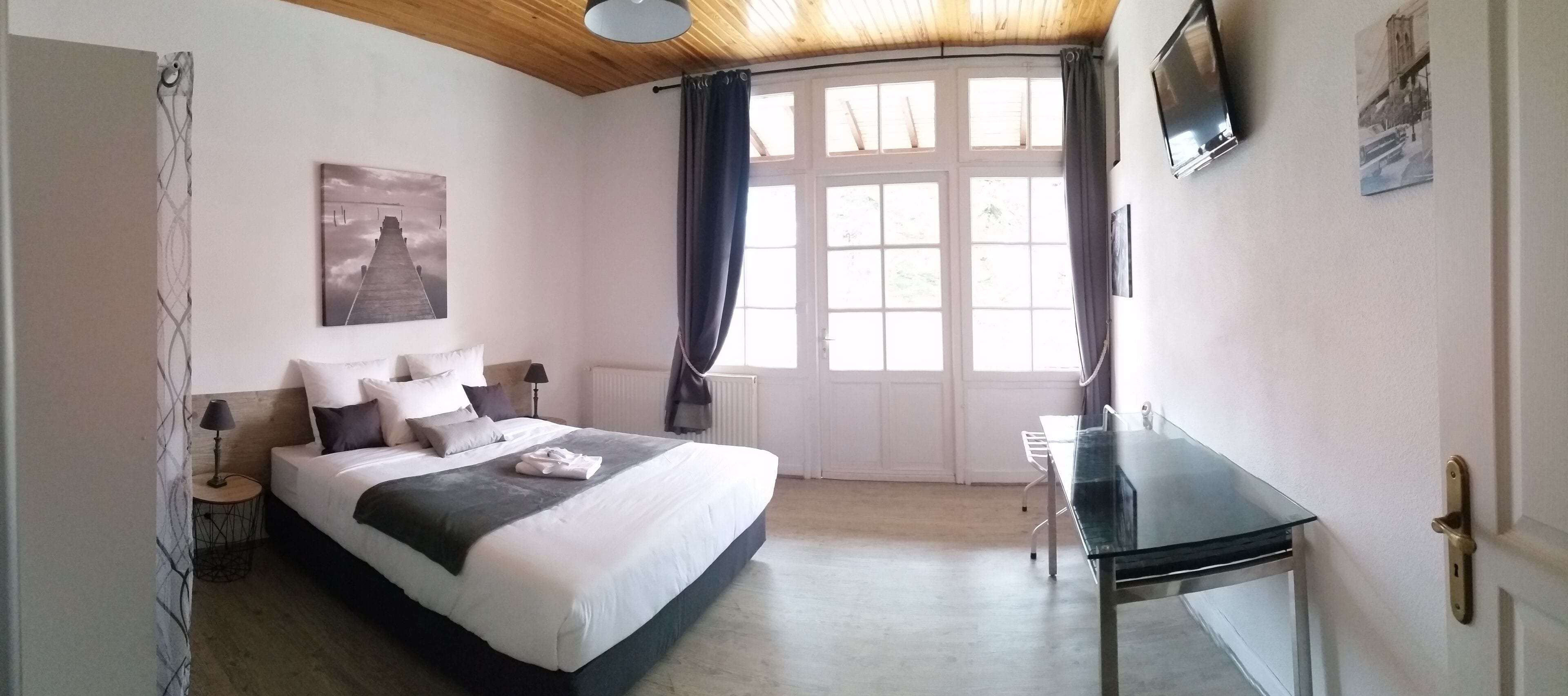 A bedroom with a bed, a desk, a TV, and a window with curtains.