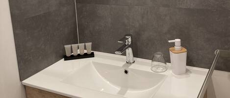 A modern bathroom with a large mirror, a white sink, a shower, and a wooden cabinet.