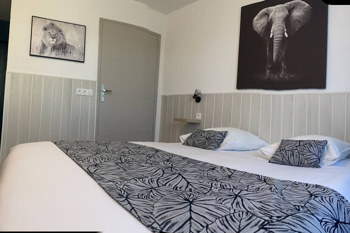 Une chambre d’hôtel avec un grand lit, une porte, un tableau représentant un éléphant accroché au mur et un luminaire fixé au mur.