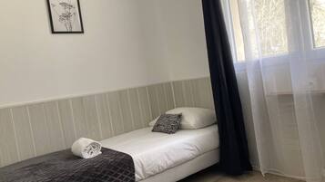 Un letto singolo con un materasso bianco, una coperta scura a motivi e un cuscino con disegno bianco e nero. Sopra il letto è appesa una foto incorniciata.